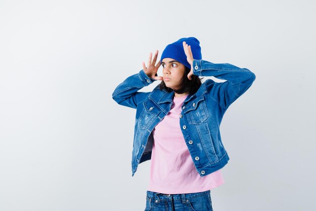 Mulher adolescente de mãos dadas perto da cabeça com um gorro de jaqueta jeans de t-shirt rosa parecendo assustada