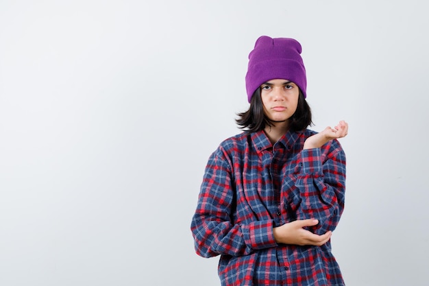 Mulher adolescente levantando a mão de forma intrigada com um gorro parecendo confuso