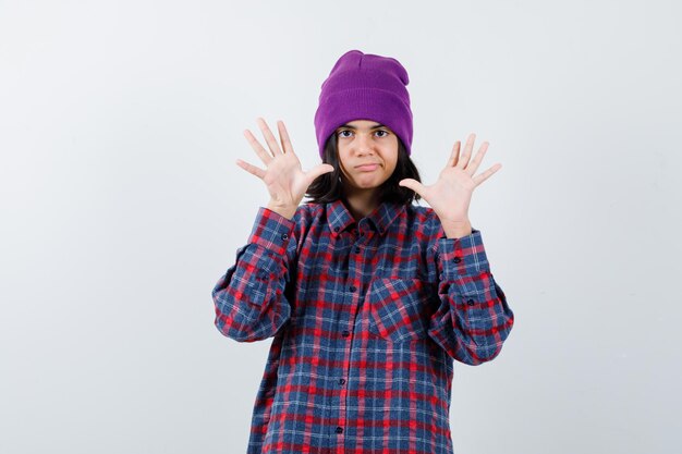 Mulher adolescente levantando as mãos em gesto de rendição. Gorro parecendo imprudente