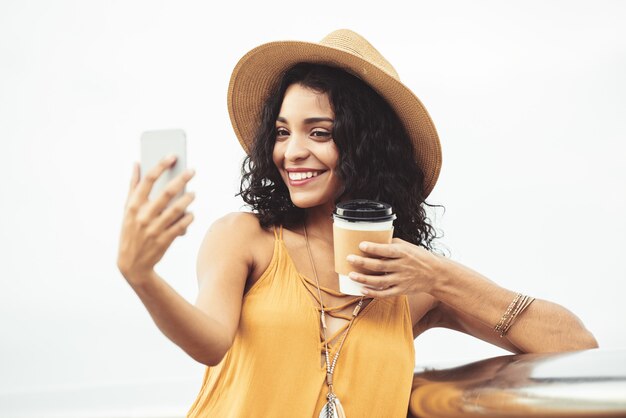 Mulher adorável com café para viagem, tendo selfie ao ar livre