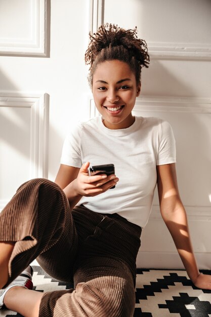 Mulher adorável com smartphone sentada no chão