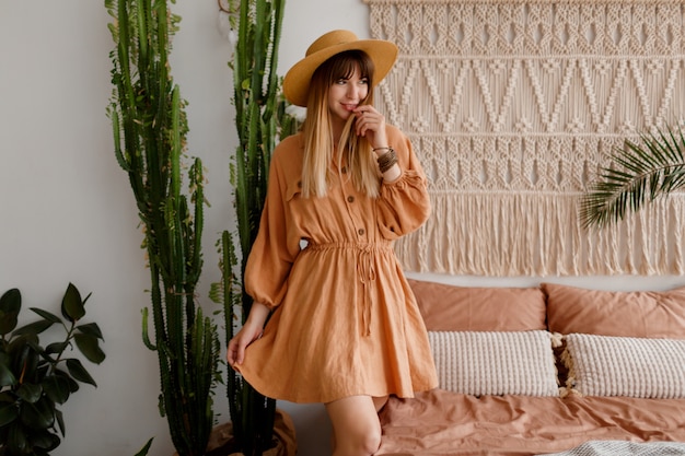 Foto grátis mulher adorável vestido de linho e chapéu de palha posando no apartamento de estilo boho