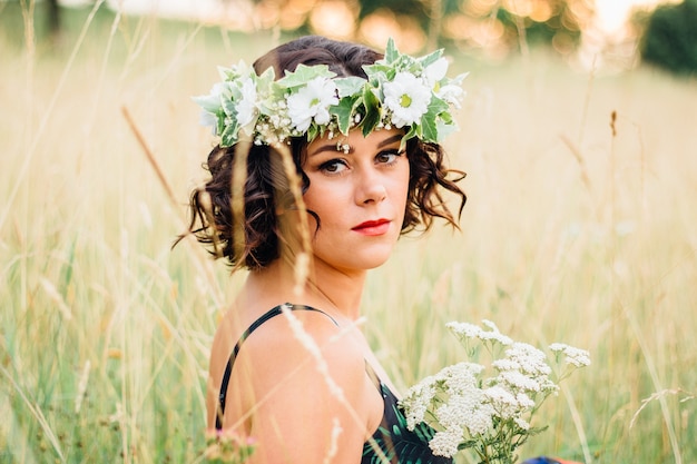 Mulher adulta com um vestido floral com uma coroa de flores na cabeça e posando em um campo