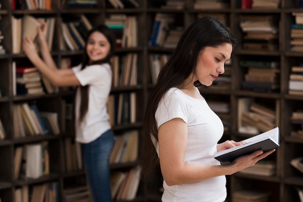 Mulher adulta e menina procurando livros na biblioteca