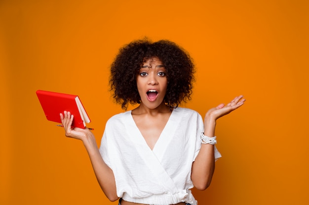 Mulher africana com cara de surpresa segurando o caderno. Emoções engraçadas.