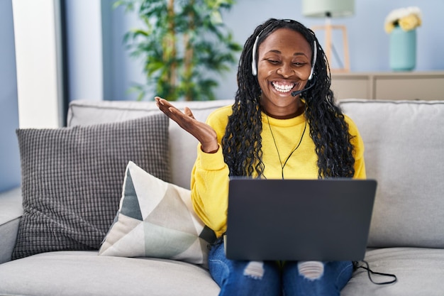 Mulher africana trabalhando em casa usando fone de ouvido do operador comemorando conquista com sorriso feliz e expressão vencedora com a mão erguida
