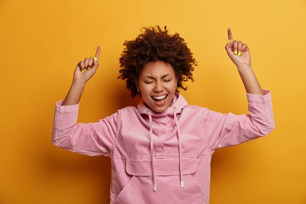 Mulher afro-americana alegre e otimista levantando as mãos e apontando para cima