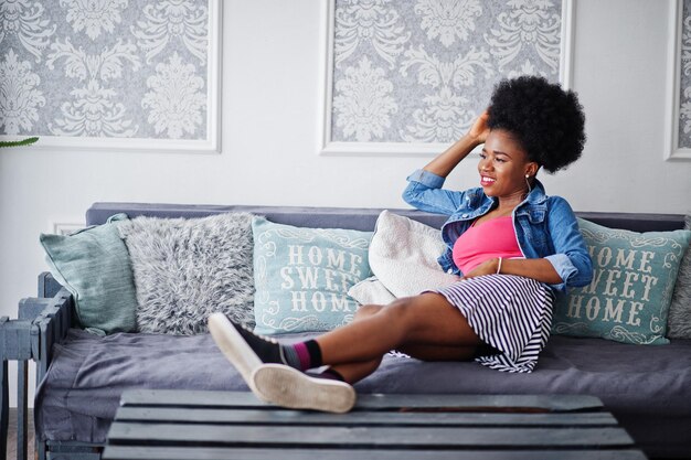 Mulher afro-americana atraente com cabelo afro desgaste na saia rosa top posada no quarto branco Modelo preto sexy na moda