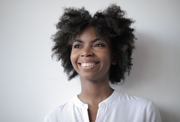 Foto grátis mulher afro-americana atraente com um sorriso largo de pé na parede branca