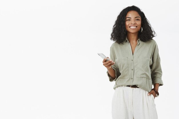 mulher afro-americana charmosa carismática com penteado encaracolado segurando a mão no bolso usando smartphone