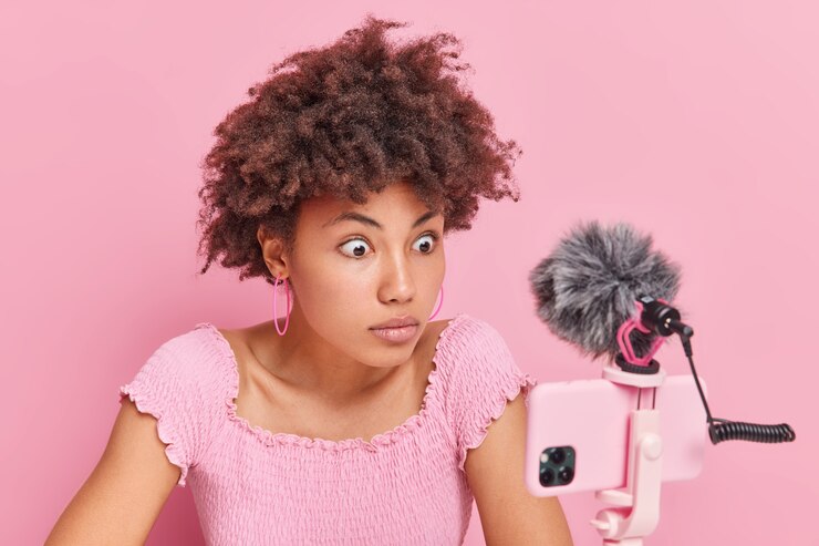 Foto grátis mulher afro-americana chocada com cabelo encaracolado olha fixamente para a webcam do telefone grava a transmissão ao vivo de vídeo tem cursos de treinamento online