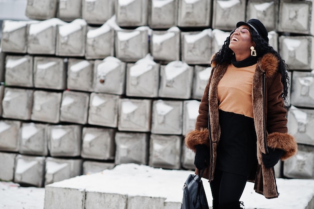 Foto grátis mulher afro-americana com casaco de pele de carneiro e boné posou no dia de inverno contra o fundo de pedra nevado