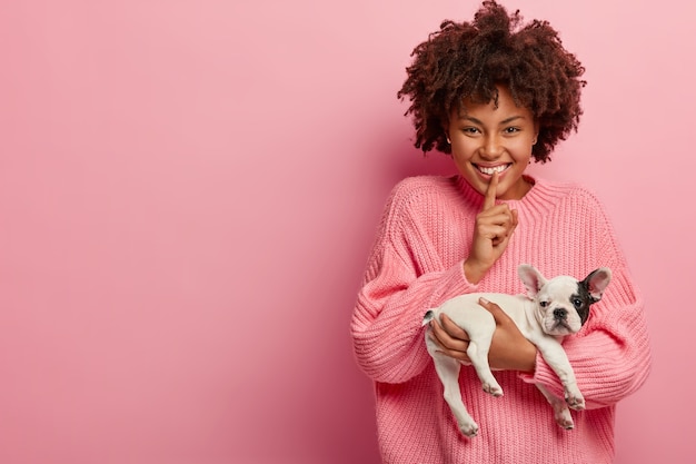 Mulher afro-americana com suéter rosa segurando um cachorrinho