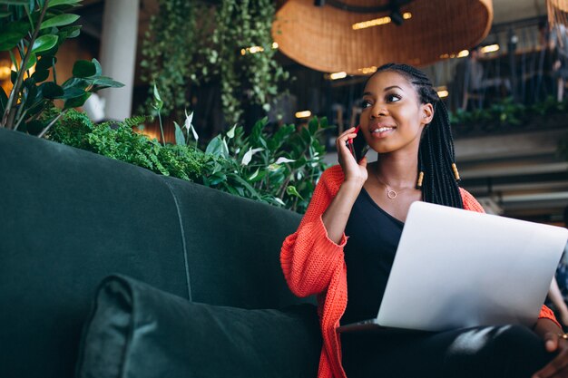 Mulher afro-americana com telefone e laptop em um café