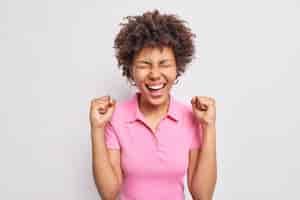 Foto grátis mulher afro-americana de cabelos cacheados feliz faz o punho balançar e se regozija resultados positivos usa camiseta rosa casual