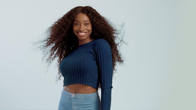 Mulher afro-americana de raça mista de beleza com cabelo soprado no ar sorrindo para a câmera dançando