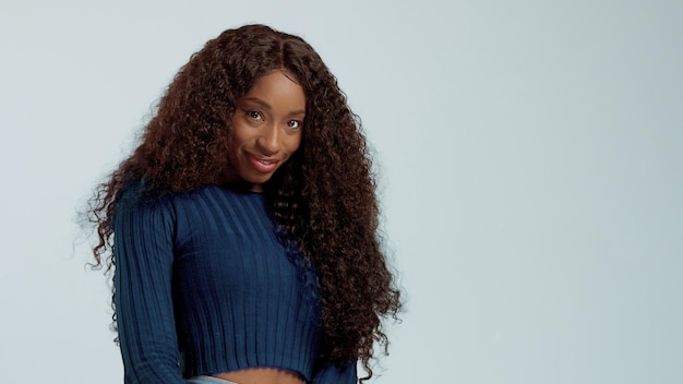 Mulher afro-americana de raça negra de beleza com cabelos longos e encaracolados e sorriso perfeito olhando para a câmera e sorrindo em azul