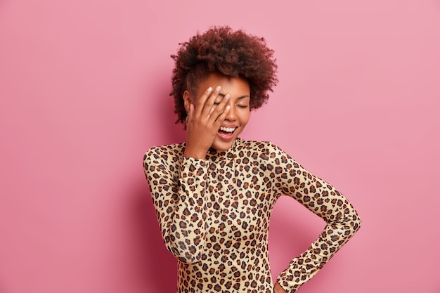 Mulher afro-americana despreocupada e positiva fazendo cara de palma, rindo positivamente, mantendo os olhos fechados, sorrindo com os dentes