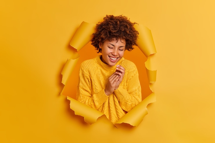 Foto grátis mulher afro-americana encaracolada feliz aperta as mãos, sorri amplamente e ri positivamente