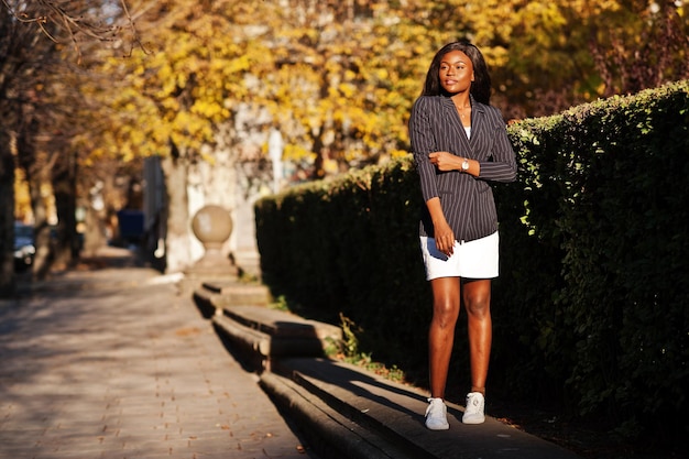 Mulher afro-americana estilosa de sucesso na jaqueta e saia posou no dia ensolarado do outono na rua