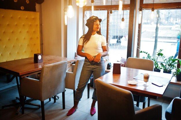 Mulher afro-americana na moda em boné preto relaxando no café aconchegante