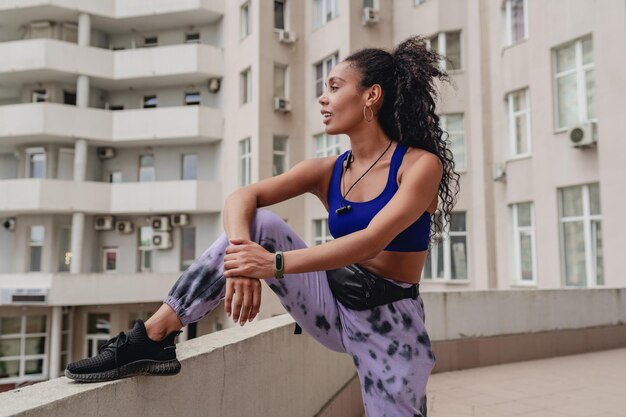 Mulher afro-americana negra atraente no esporte fitness roupa urbana no telhado fazendo exercícios confiantes estilo de cabelo encaracolado corpo atlético músculos fortes