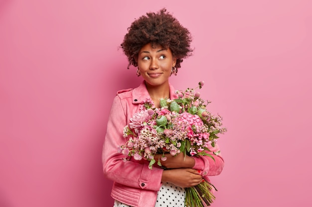 Mulher afro-americana pensativa com lindo buquê de flores, vestida com roupas da moda,