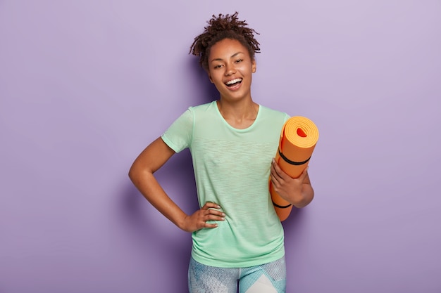 Foto grátis mulher afro positiva em forma física faz exercícios físicos e malha em casa, segura karemat laranja