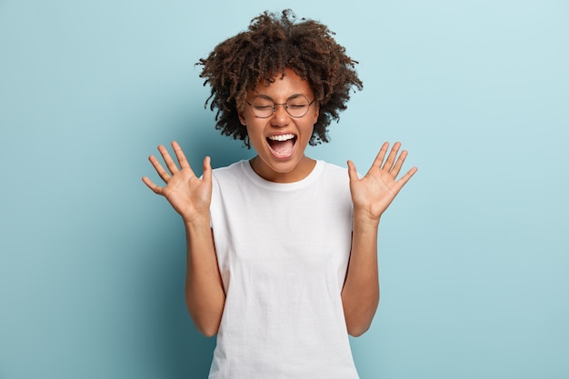 Mulher afro superemotiva ri alto, ouve uma piada ou história engraçada, levanta as palmas das mãos com satisfação