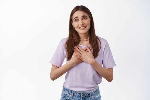 Foto grátis mulher agradecendo por algo bom, mãos no peito e sorrindo, agradeço ajuda, grata, pisando em branco