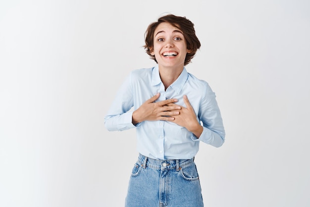 Mulher agradecida feliz tocando o peito e sorrindo agradecendo a ajuda que fica satisfeita em fundo branco