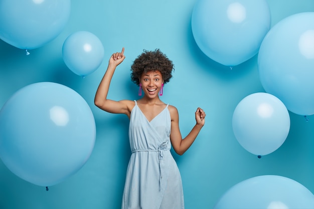 Mulher alegre alegre e festiva com sorriso hollywood, ri de alegria, move-se despreocupada e dança ao som da música, se diverte, faz feliz foto de feriado, comemora aniversário, rodeada de balões.