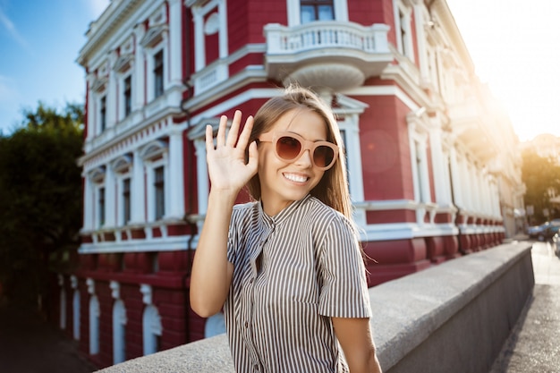 Foto grátis mulher alegre bonita jovem em óculos de sol andando pela cidade, sorrindo.
