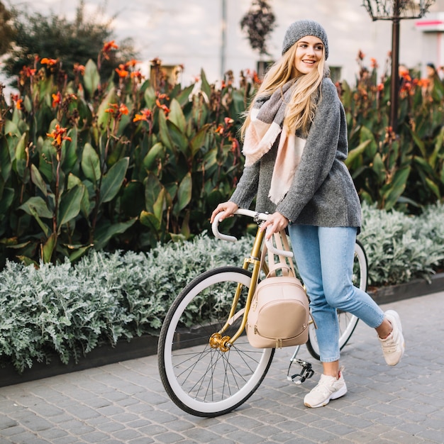 Mulher alegre caminhando com bicicleta perto de um talo de flores