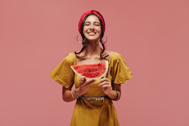 Mulher alegre e elegante com penteado descolado em bandana brilhante, brincos redondos de prata e vestido de verão amarelo posando com os olhos fechados