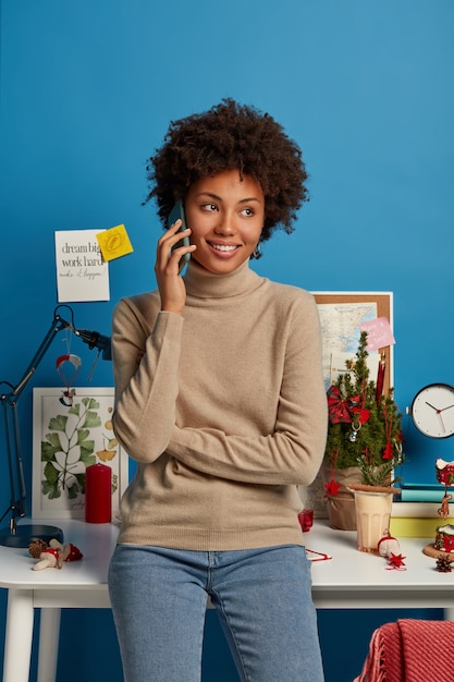 Foto grátis mulher alegre e encaracolada conversa ao telefone, vestida com roupa casual, olha de lado com um sorriso cheio de dentes