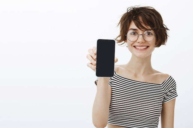 Mulher alegre e hipster apresenta o aplicativo, mostrando a tela do smartphone