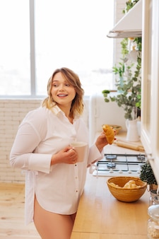 Mulher alegre e simpática sorrindo enquanto pega um croissant da cesta na cozinha