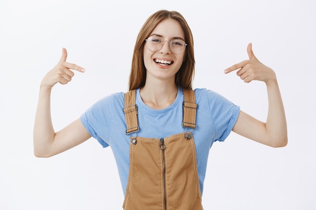 Mulher alegre e sorridente de óculos apontando para si mesma ou para o logotipo