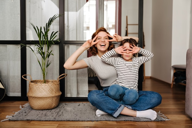 Foto grátis mulher alegre e sua filha se divertindo na sala e dando sinais de paz.