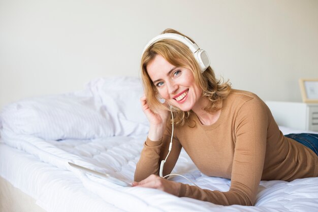 Mulher alegre em fones de ouvido, ouvindo música na cama