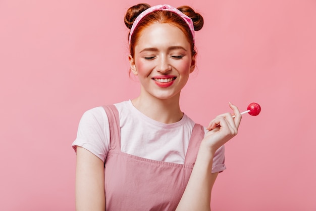 Mulher alegre em t-shirt branca e top sorrisos e detém doces no fundo rosa.