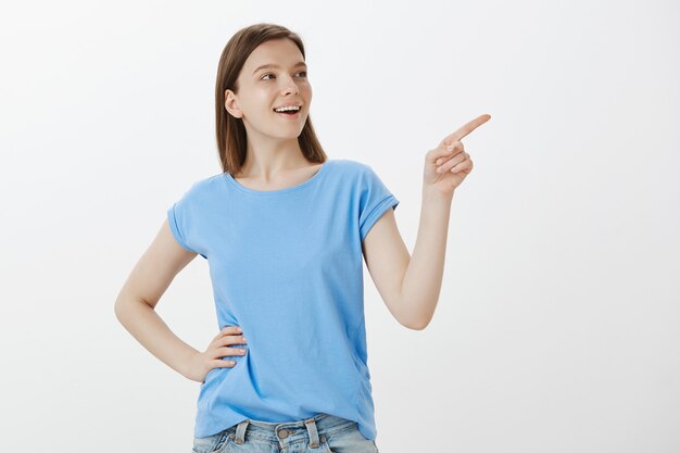 Mulher alegre em uma camiseta azul apontando para o canto superior direito, mostrando seu logotipo