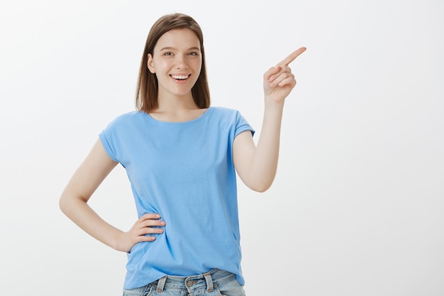 Mulher alegre em uma camiseta azul apontando para o canto superior direito, mostrando seu logotipo
