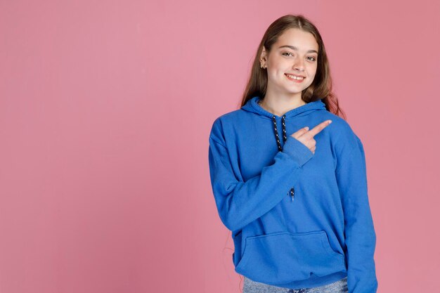 Mulher alegre mostrando direção com a mão direita gesticulando enquanto sinceramente sorrindo para a câmera