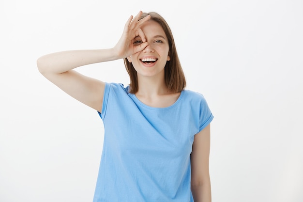 Mulher amigável e despreocupada rindo feliz e mostrando sinal de ok sobre o olho, tudo bem, tudo perfeito