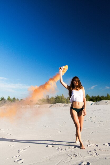 Mulher anda com fumaça na praia branca sob o céu azul