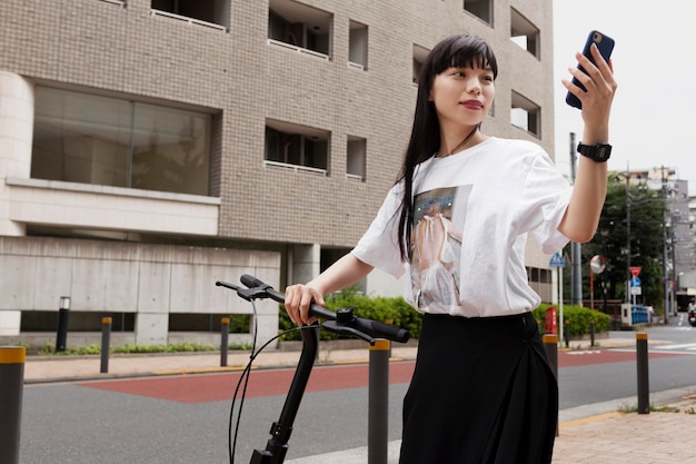 Mulher andando de bicicleta elétrica na cidade e segurando um smartphone