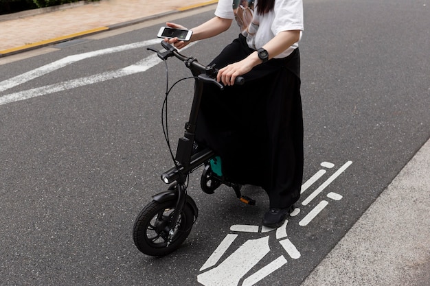 Mulher andando de bicicleta elétrica na cidade e segurando um smartphone