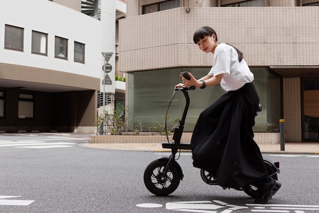 Mulher andando de bicicleta elétrica na cidade e segurando um smartphone